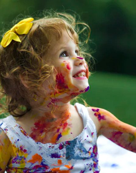 smiling young girl with bright colored paint on her face and clothes